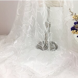 May include: White sheer fabric with an embroidered floral pattern. The fabric is delicate and has a soft, flowing texture.