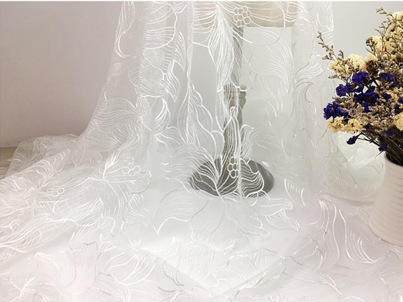 May include: White sheer fabric with an embroidered floral pattern. The fabric is delicate and has a soft, flowing texture.