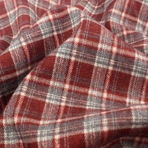 May include: A fabric featuring a classic plaid pattern in deep red, charcoal gray, and thin white intersecting lines. The material is folded, creating soft, organic curves and shadows that highlight the texture and the repeating checkered design.