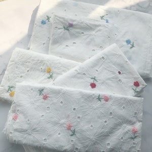 May include: White cotton fabric with a delicate floral pattern and small embroidered flowers in various colors, including pink, yellow, red, and blue.