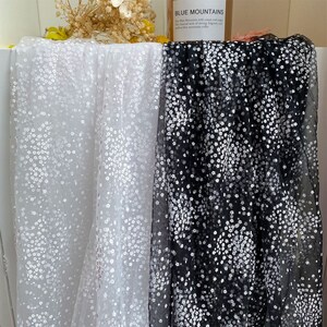 以下が含まれることがあります： 黒と白の背景に白い花柄が施された、透き通った生地が2枚。生地は透き通っていて、繊細で軽い感触です。