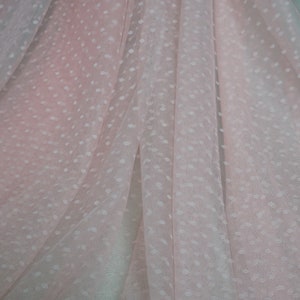 Puede incluir: Tela transparente rosa p&aacute;lido con un patr&oacute;n de lunares blancos. La tela est&aacute; doblada y drapeada, mostrando la textura y el patr&oacute;n.
