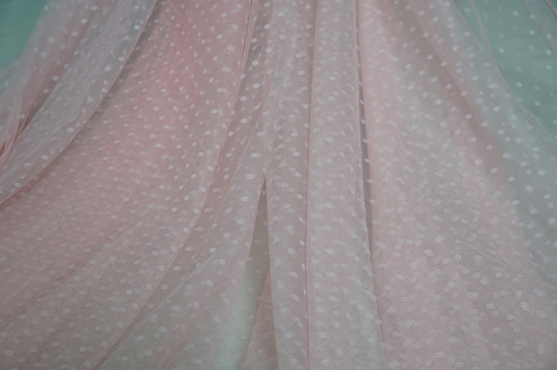 Puede incluir: Tela transparente rosa p&aacute;lido con un patr&oacute;n de lunares blancos. La tela est&aacute; doblada y drapeada, mostrando la textura y el patr&oacute;n.