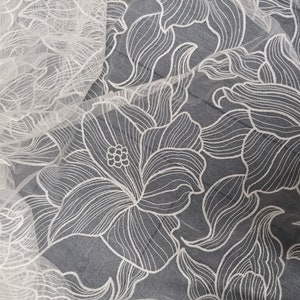 May include: White floral lace fabric with a delicate, intricate design. The lace is sheer and has a soft, flowing texture.