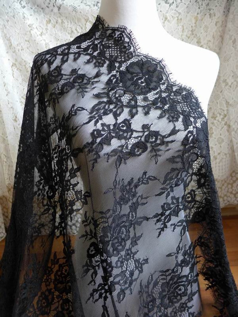 May include: Black lace fabric with a floral pattern. The lace has a scalloped edge.