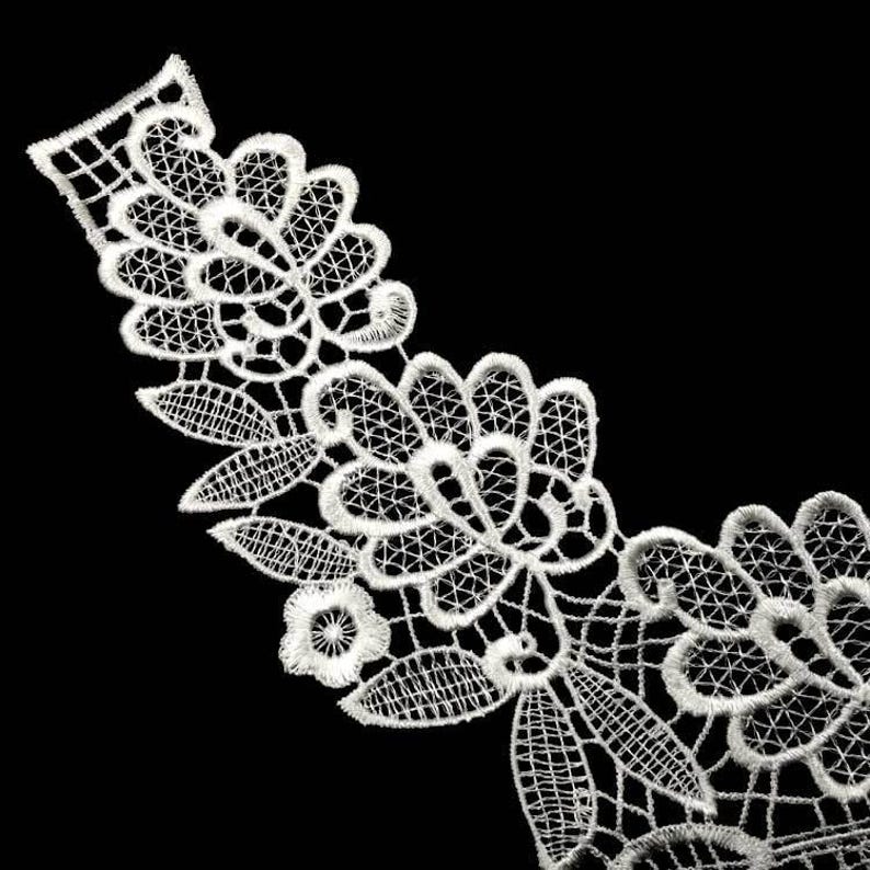 Pu&ograve; includere: Bordino in pizzo bianco con un motivo floreale. Il pizzo &egrave; delicato e intricato, con un bordo a festoni.