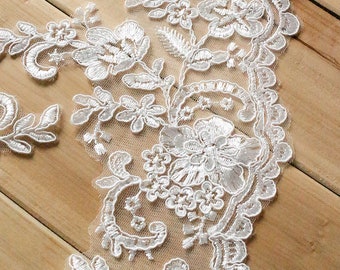 May include: White lace trim featuring a floral design. The lace has a delicate, intricate pattern with small flowers and leaves.