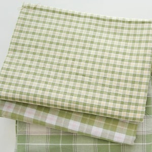 Pode incluir: Três peças de tecido xadrez verde e branco. A peça superior é um xadrez verde claro e branco, a peça do meio é um xadrez verde escuro e branco com uma faixa rosa, e a peça inferior é um xadrez verde escuro e branco.