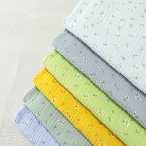May include: A stack of colorful cotton fabric with a crinkled texture. The fabric is in shades of blue, green, and yellow, each adorned with a delicate floral pattern in white and red. The layers are neatly arranged, showcasing the variety of colors and designs.