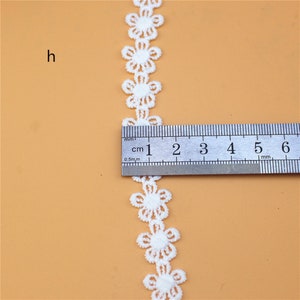 May include: White lace trim with a repeating flower design. The trim is measured with a ruler, showing it is about 1 inch wide.