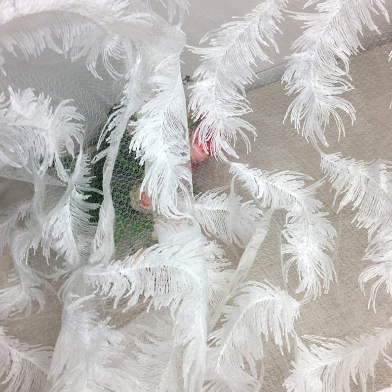 May include: White sheer fabric with a delicate feather design. The fabric is soft and airy, making it perfect for curtains, tablecloths, or other decorative purposes.