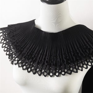 Könnte beinhalten: Schwarze Spitzenkragen mit einem gewellten Rand und einem plissierten Design. Der Kragen ist aus einem leichten Stoff gefertigt und hat einen zarten, femininen Look.