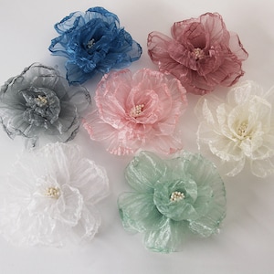 May include: Six fabric flowers in various colours, including pink, blue, white, green, and grey. The flowers are made of layered tulle and have a delicate, ruffled appearance.