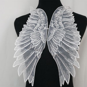 May include: A pair of white lace angel wings with a detailed feather design. The wings are attached to a black mannequin.