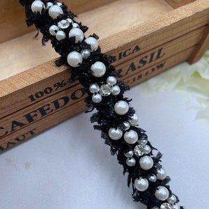 Puede incluir: Ribete negro con cuentas, perlas de imitaci&oacute;n y detalles de pedrer&iacute;a. El ribete est&aacute; hecho de una tela negra texturizada y decorado con perlas de imitaci&oacute;n blancas y peque&ntilde;os brillantes. Ideal para proyectos de manualidades.