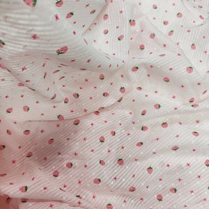 May include: Pink sheer fabric with a white stripe pattern and a small pink strawberry print.