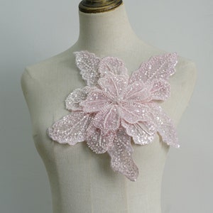 Op de afbeelding: Een delicaat roze bloemvormig versiering gemaakt van pailletten en kralen. Dit decoratieve stuk is perfect om een ​​toets van elegantie toe te voegen aan kleding, accessoires of doe-het-zelfprojecten voor thuis.