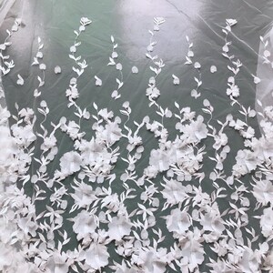 May include: White floral lace fabric with 3D flowers and leaves. The fabric has a sheer, delicate texture and is perfect for adding a touch of elegance to any project.