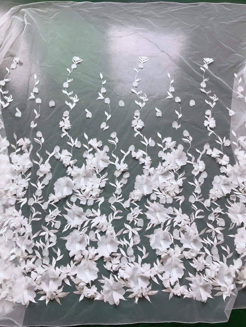 May include: White floral lace fabric with 3D flowers and leaves. The fabric has a sheer, delicate texture and is perfect for adding a touch of elegance to any project.