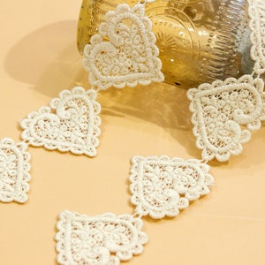 May include: A white crocheted lace trim with a repeating heart design. The trim is made of delicate, intricate lace and is perfect for adding a touch of elegance to any project.