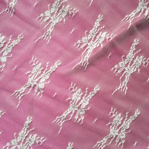May include: White lace fabric with a floral pattern on a pink background.