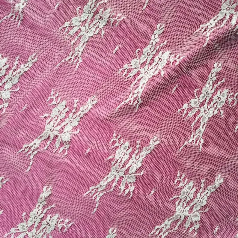 May include: White lace fabric with a floral pattern on a pink background.