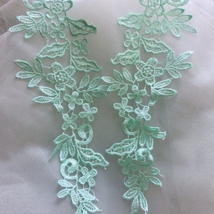 May include: Two delicate mint green lace appliques featuring floral and leaf designs. The appliques are ideal for adding a touch of elegance to clothing, crafts, or home decor.