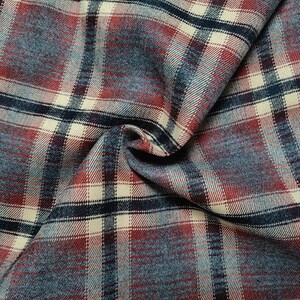 Puede incluir: Primer plano de una tela doblada con un patrón de cuadros. La tela presenta una mezcla de colores, incluyendo rojo, azul, crema y marino. El diseño de cuadros se compone de líneas verticales y horizontales que se cruzan, creando un aspecto clásico y texturizado. La tela parece suave y posiblemente de franela.
