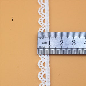 May include: White lace trim with a scalloped edge, measured against a ruler showing 1 centimeter.