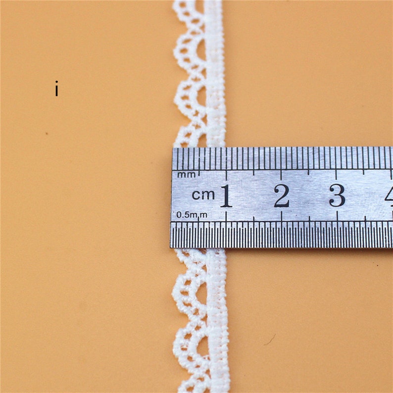 May include: White lace trim with a scalloped edge, measured against a ruler showing 1 centimeter.