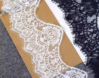 May include: Close-up of white and black lace trim. The white lace is on a brown surface, while the black lace is on a white surface. Both trims have a floral design and scalloped edges. The lace is likely used for sewing or crafting.