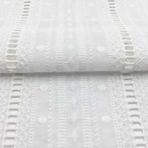 May include: White cotton fabric with an embroidered pattern of geometric shapes and small circles. The fabric has a delicate, lacy look.