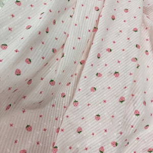 May include: Pink fabric with a white and pink striped pattern and a repeating pattern of small pink flowers and pink strawberries.
