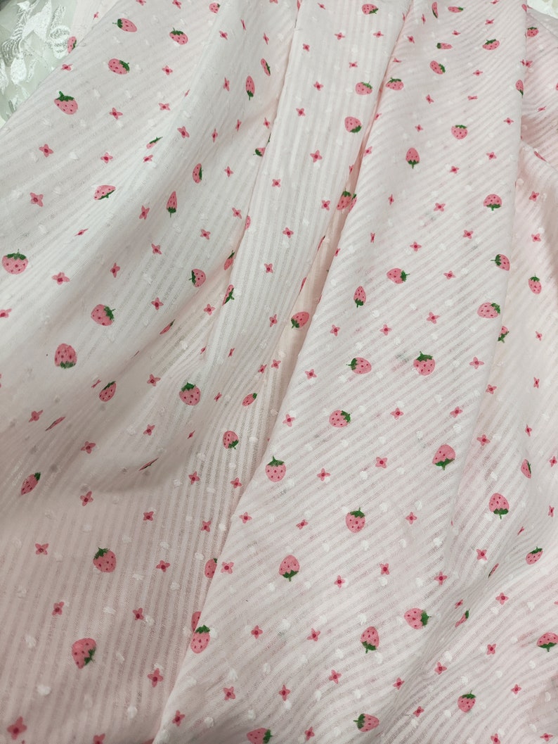 May include: Pink fabric with a white and pink striped pattern and a repeating pattern of small pink flowers and pink strawberries.