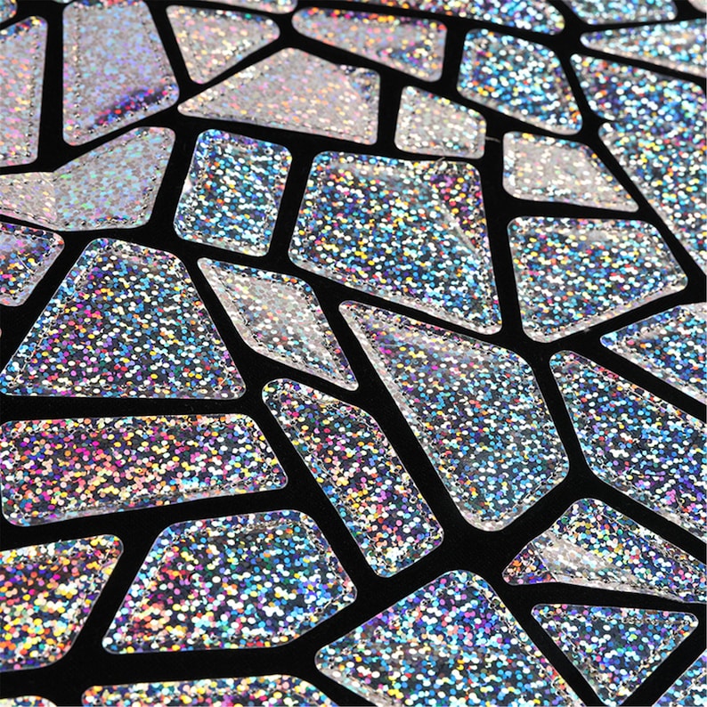 K&ouml;nnte beinhalten: Nahaufnahme eines schwarzen Stoffes mit einem geometrischen Muster aus silbernen, glitzernden Formen.