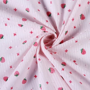 May include: Pink fabric with a white polka dot pattern and a repeating pattern of red strawberries and small white flowers.
