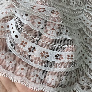 May include: White lace fabric with a delicate floral pattern. The lace has a scalloped edge and is perfect for crafting projects.