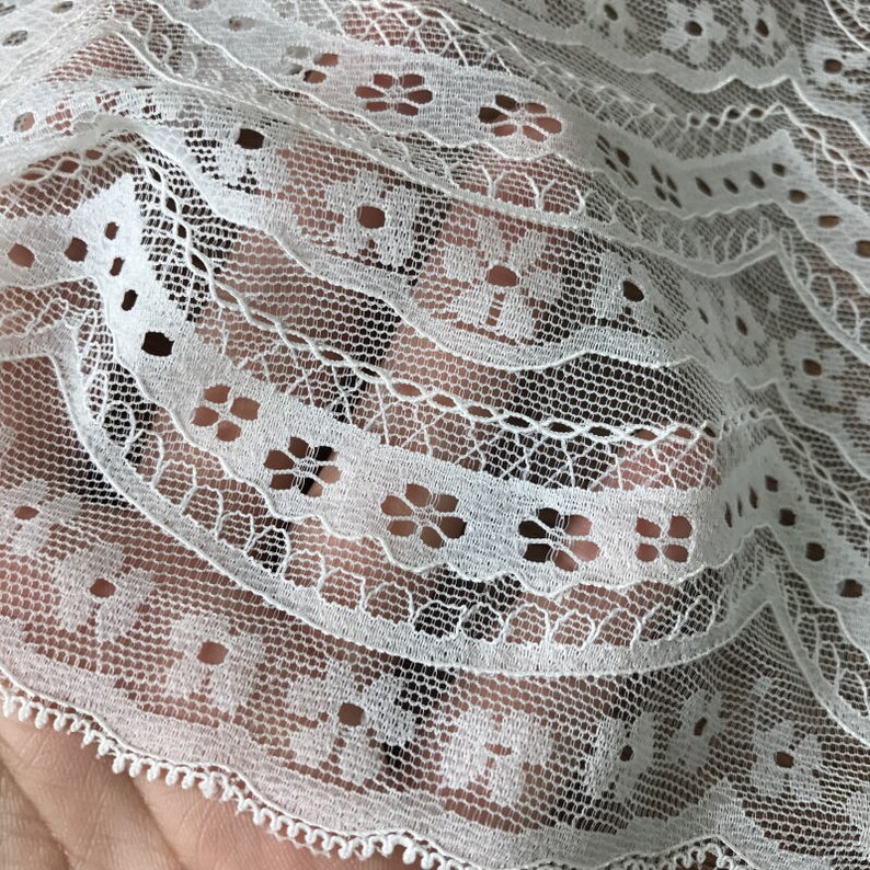 May include: White lace fabric with a delicate floral pattern. The lace has a scalloped edge and is perfect for crafting projects.