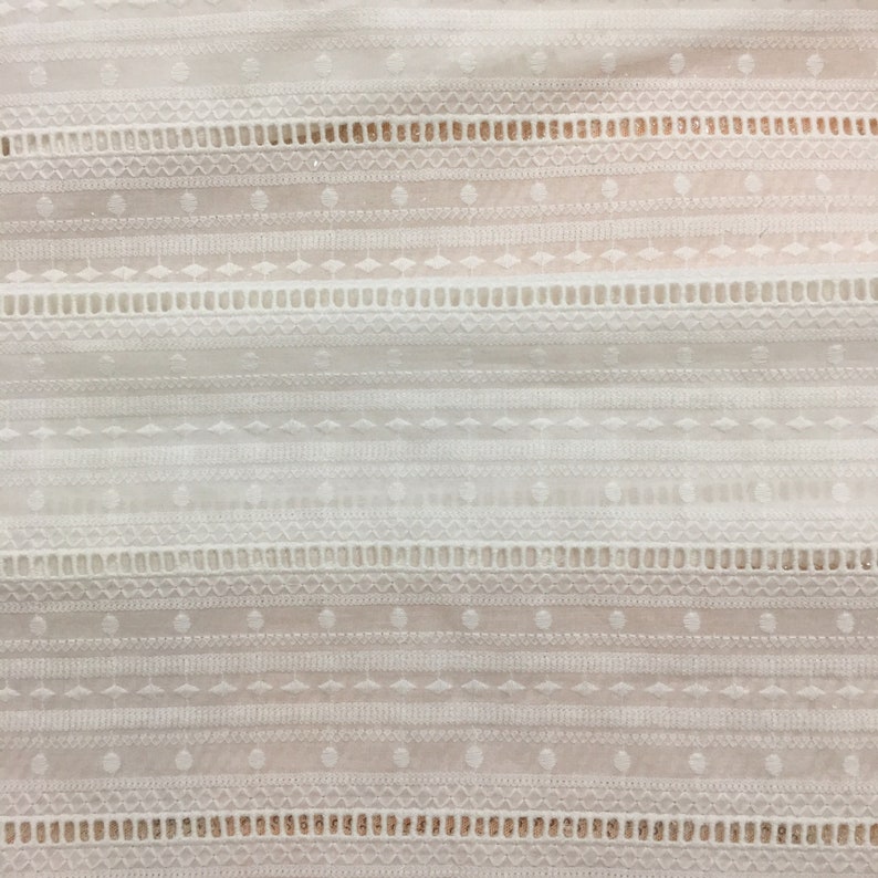 May include: White cotton fabric with a delicate embroidered pattern of geometric shapes and lines. The fabric has a subtle sheen and a soft texture.