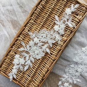 Może przedstawiać: Biała koronka ozdobiona perełkami i kwiatowymi wzorami. Koronka jest prezentowana w wiklinowym koszyku.