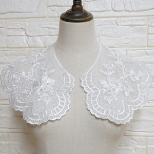 May include: White lace collar with a scalloped edge and floral embroidery. The collar is shown on a white mannequin.