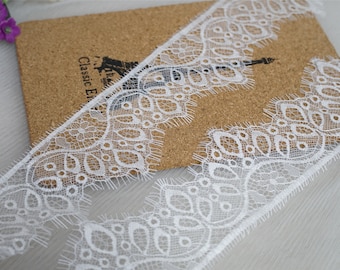 May include: White lace trim with a delicate floral pattern. The trim has a scalloped edge and a frayed finish.
