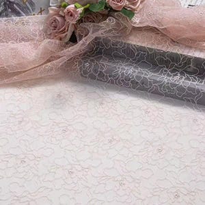 Peut inclure: Tissu en dentelle florale rose pâle avec un motif brodé délicat. Le tissu est drapé sur une surface, avec un bouquet de roses roses en arrière-plan. La dentelle présente un motif floral répété.