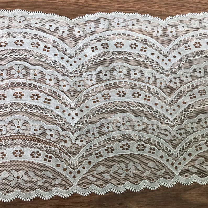 May include: White lace trim with a scalloped edge and a repeating pattern of small flowers and curved lines.