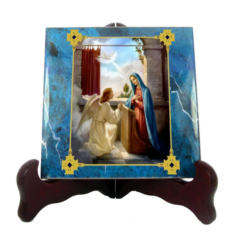 May include: A ceramic tile with a blue marble background and a gold frame. The tile features a religious image of the Annunciation, depicting the Angel Gabriel appearing to the Virgin Mary.