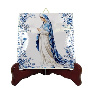 May include: A ceramic tile with a blue and white floral design featuring a depiction of the Virgin Mary in a blue robe and white dress. The tile is on a wooden stand.