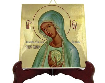 May include: A gold-toned ceramic icon of the Virgin Mary with a blue robe and a gold halo. The icon is on a wooden stand and has the text "'TOKY'O OMH'RO" in Greek.