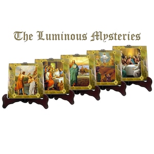 May include: Five framed images depicting scenes from the Luminous Mysteries of the Rosary. Each image is set on a wooden stand and features a different scene from the life of Jesus Christ. The images are in a gold frame with a gold background.