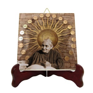 May include: A ceramic tile with a gold sunburst design and a portrait of a woman in the center. The tile has Roman numerals around the edge and is on a wooden stand.