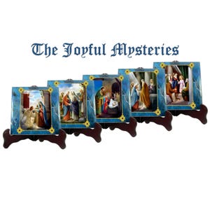 May include: Five blue and gold framed images of the Joyful Mysteries of the Rosary. Each image depicts a scene from the life of Jesus and Mary. The images are on small wooden stands.